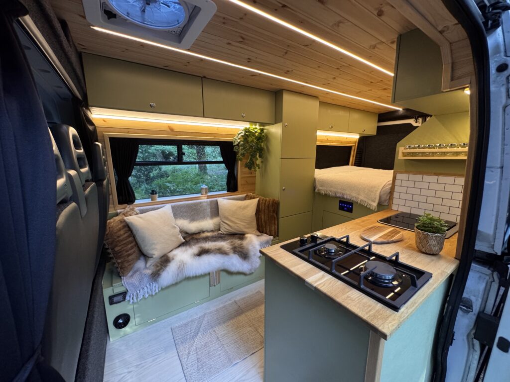 Campervan interior with olive-green cabinetry, wood finishes, seating and kitchen