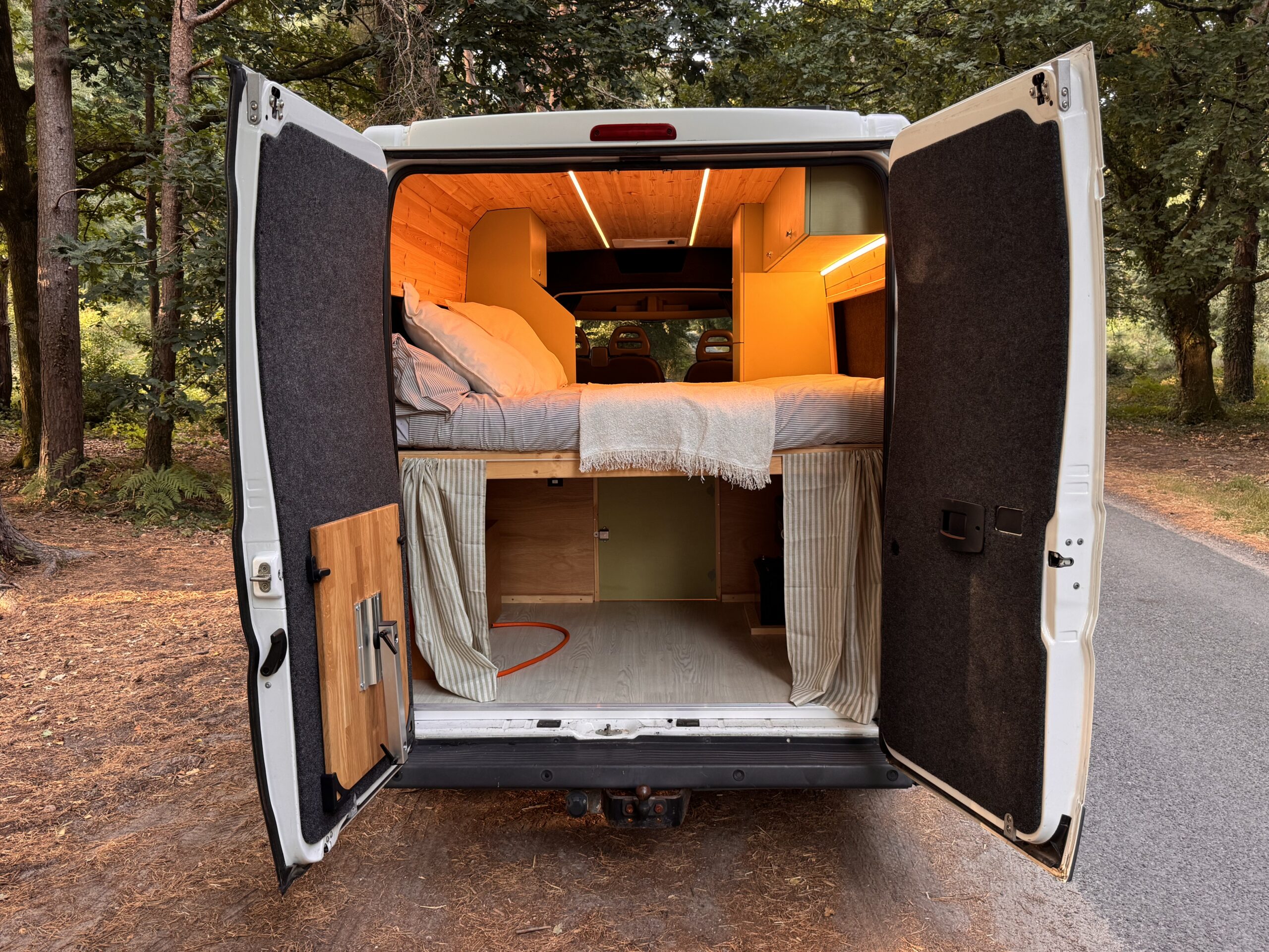 Raised rear bed inside the campervan with warm lighting and wood paneling