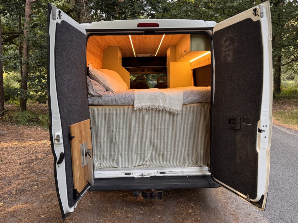 Open rear doors framing the campervan bed and warm-lit interior