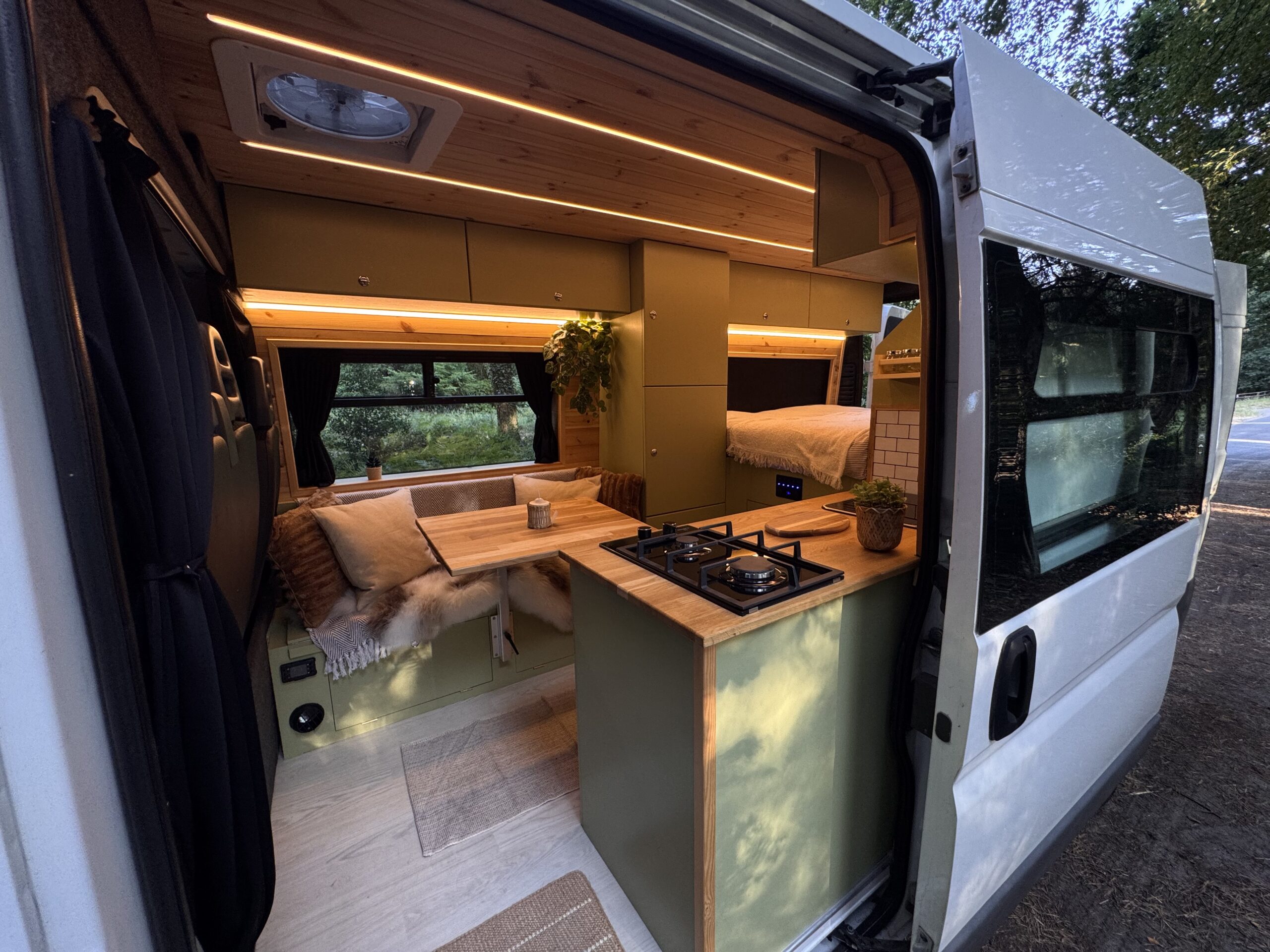 Campervan interior viewed from the rear with kitchen, seating and bed