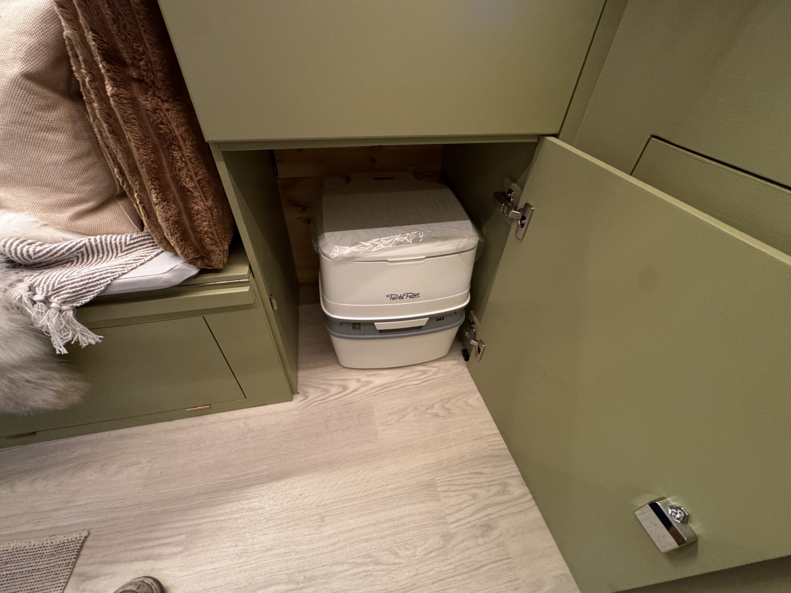 Portable toilet stored inside an olive-green campervan cabinet