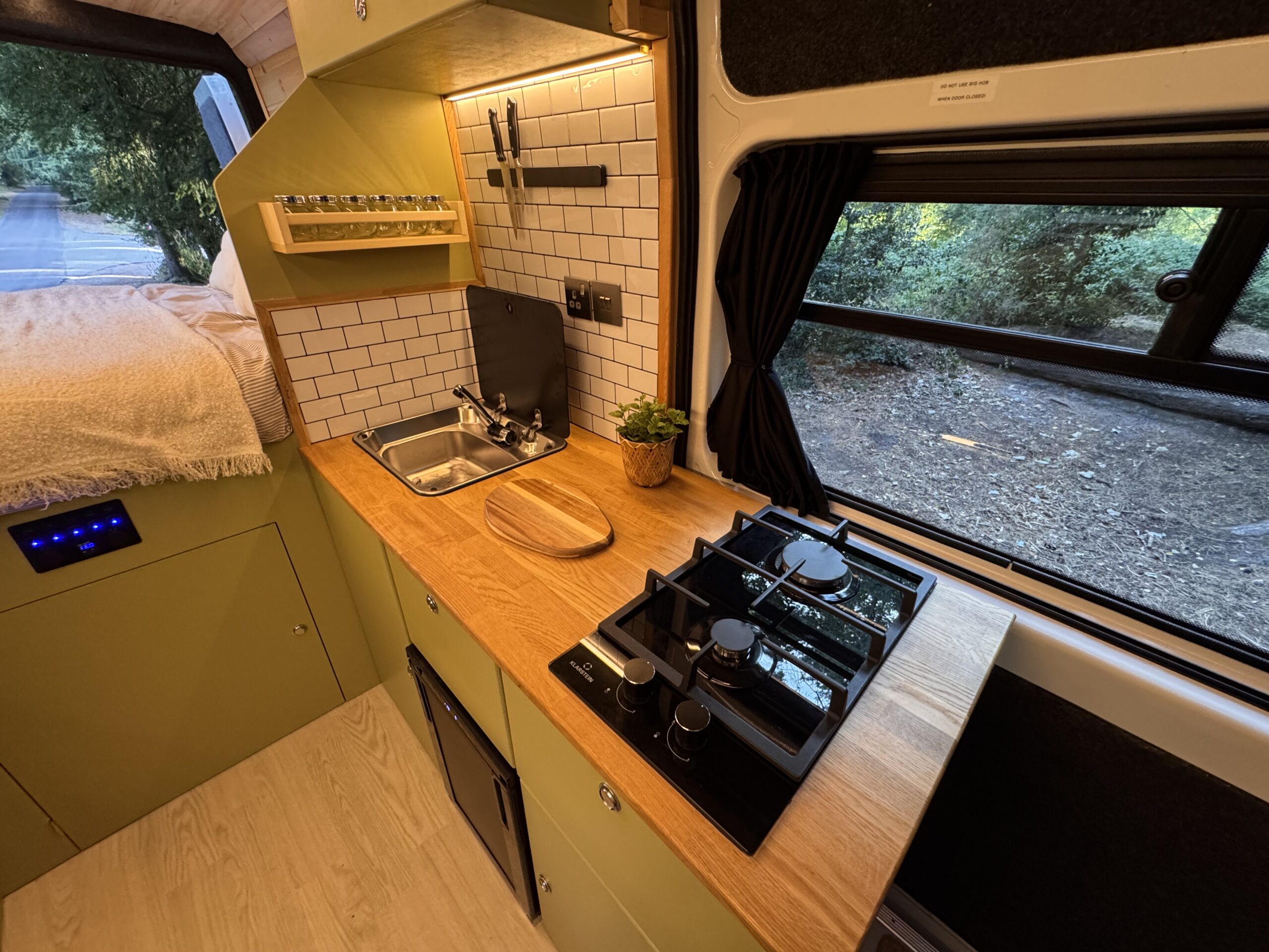 Campervan kitchen with green cabinetry, wood worktop, sink and two-burner hob